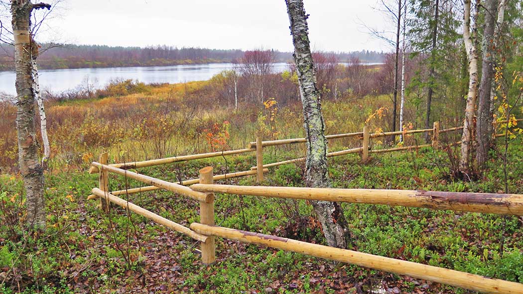 A fenced area in the foreground. An autumn lake landscape in the background.