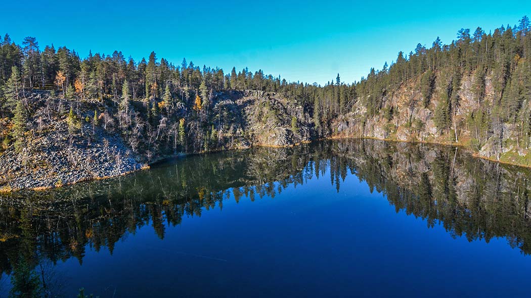 A clear lake. Cliffs and a pine forest in the background.