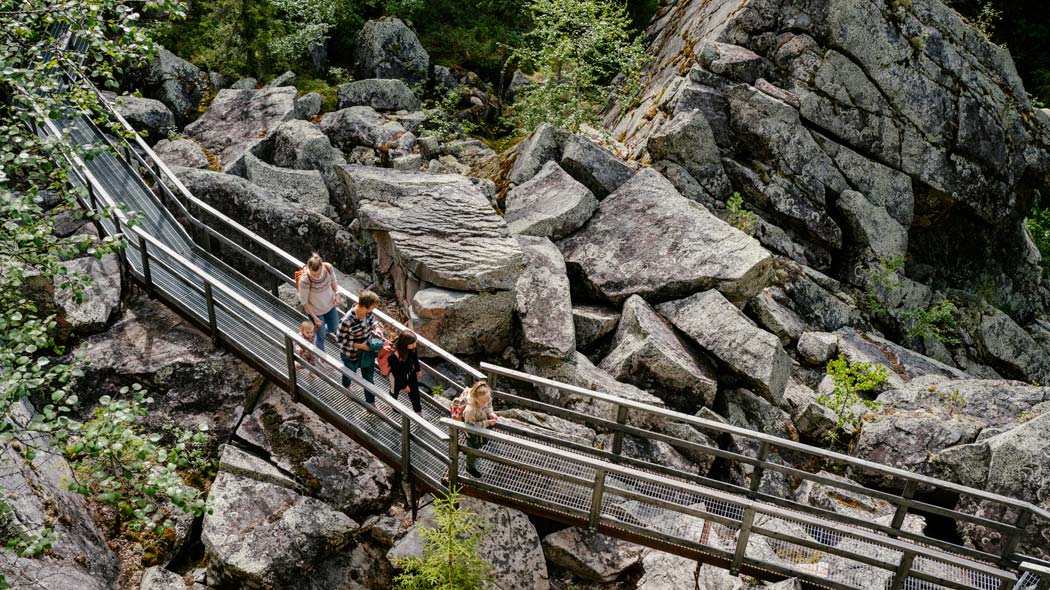 Two adults and three children walking on metal structured trail surrounded by rocky landscape.