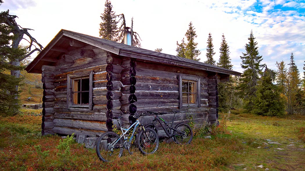 A logwood hut in autumn nature. Next to the hut wall there are two mountain bikes.