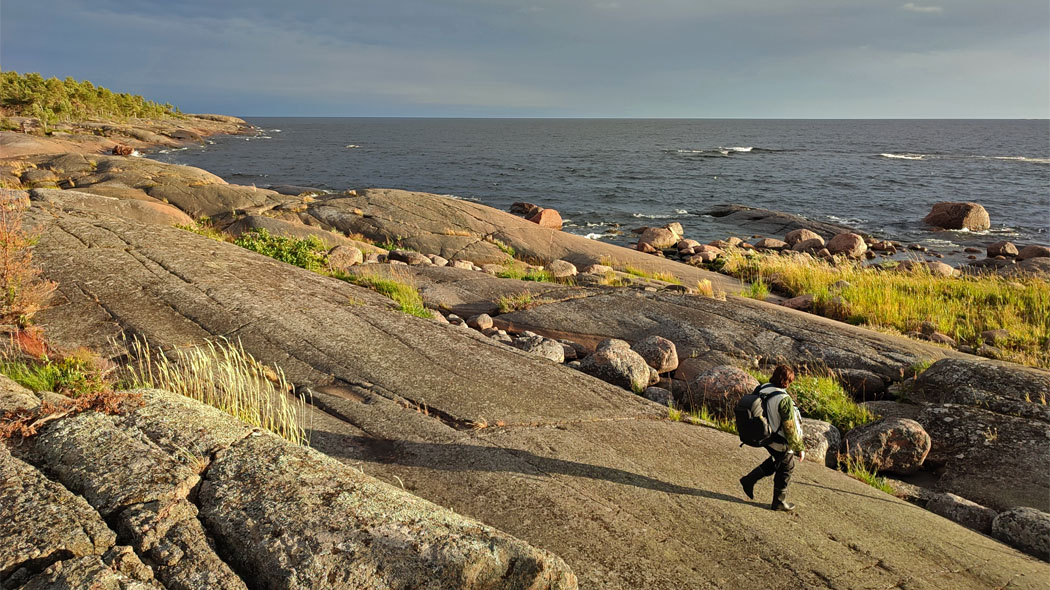Archipelago in early autumn. There is rock and a hiker in the foreground and rocky shore with some trees and the horizon in the backgroud.