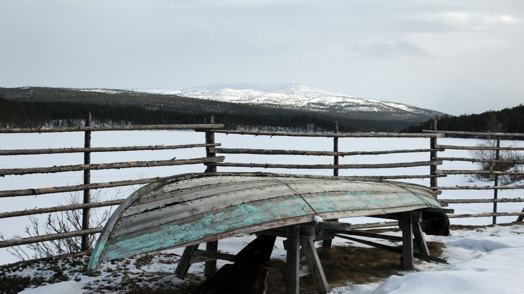A boat lie upside down in a wintry landscape. A snow-covered fell top in the background.