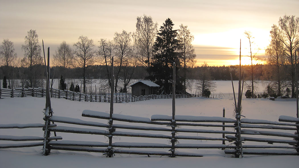 Snowy lake landscape behind a fence. Log barn by the lake.