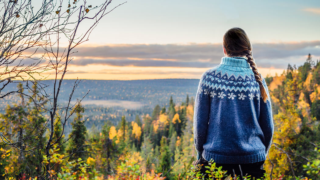 A hiker wearing a sweater stands by the autumn and colorful landscape that opens up from the danger to the back of the photographer.