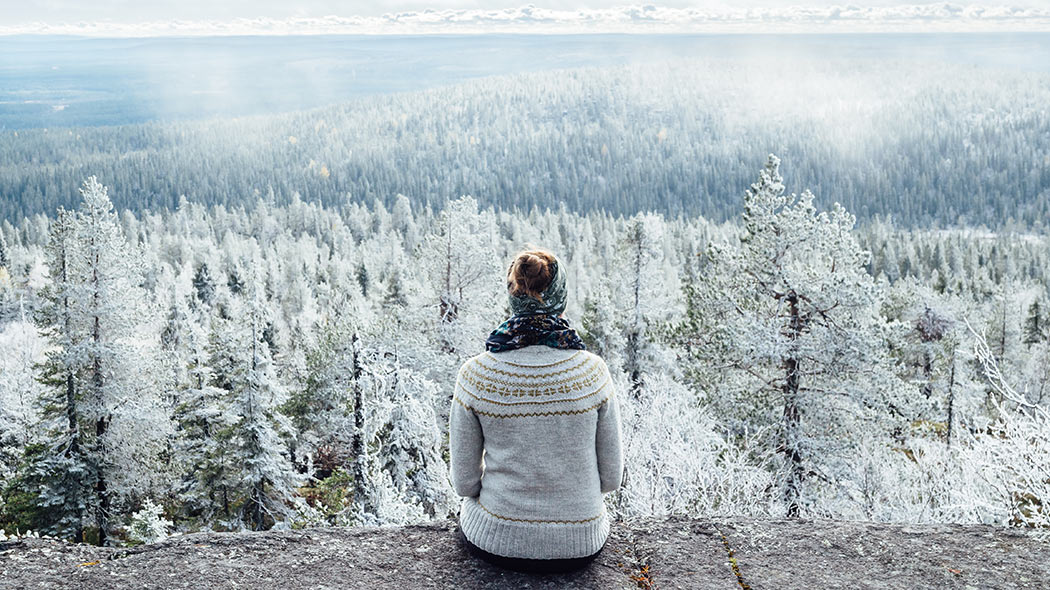 A hiker sits on a hill and looks at the winter landscape.