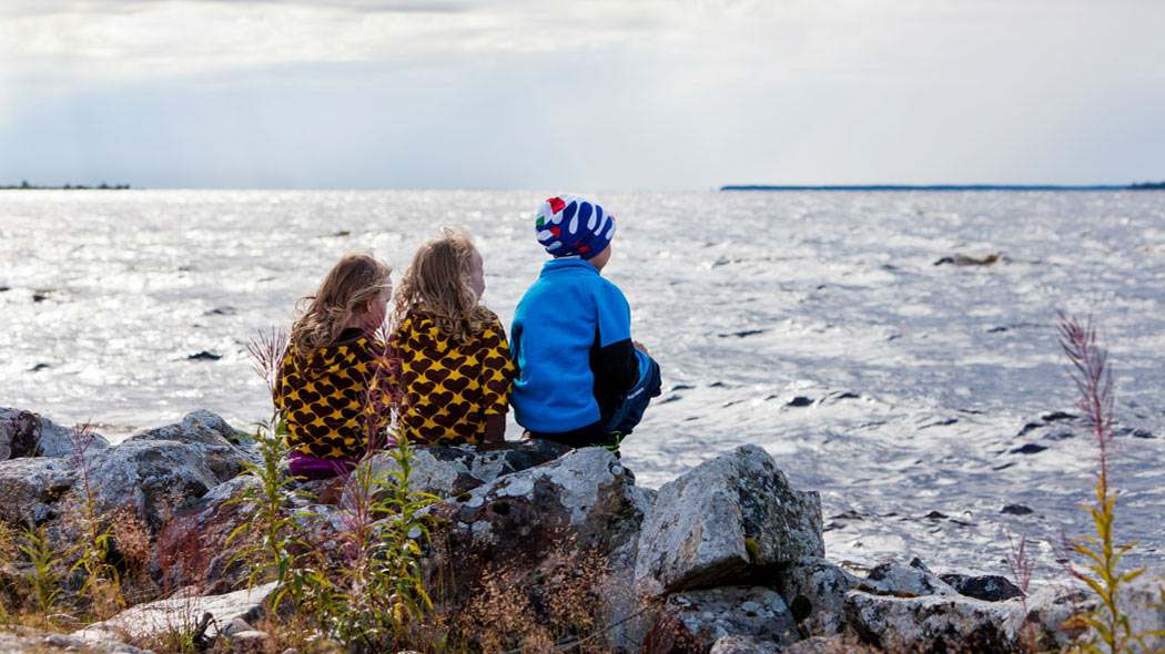Three small children are sitting on the shores and watching the undulating lake.