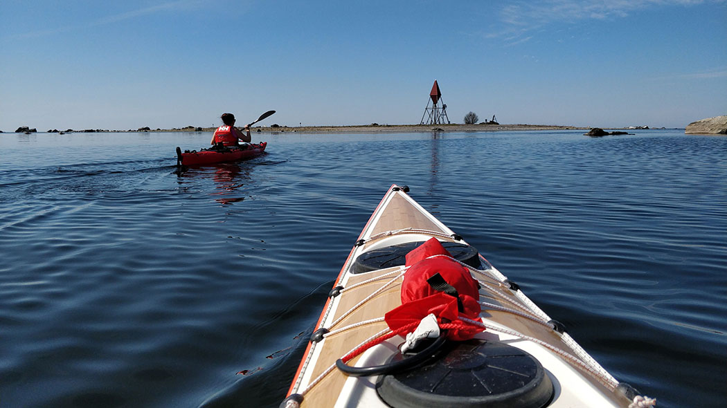 Two hikers paddling a canoe on a calm summer day. There is a low, barren island with a sea beacon in the background.
