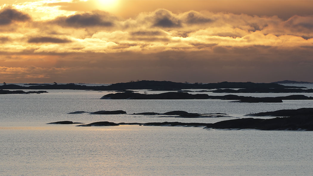 The archipelago's islets and islands as silhouettes in the backlight on a calm day.