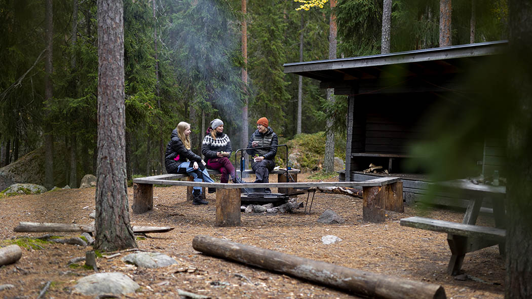 Three hikers sitting on the benches next to campfire.