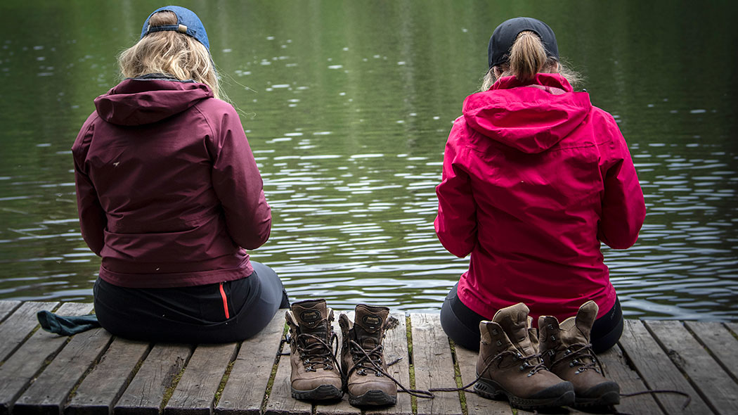 Two hikers sitting on wooden boards by the water. They have taken off their shoes.
