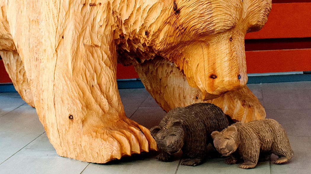 Three bears made of wood inside on the floor, one big and two small.