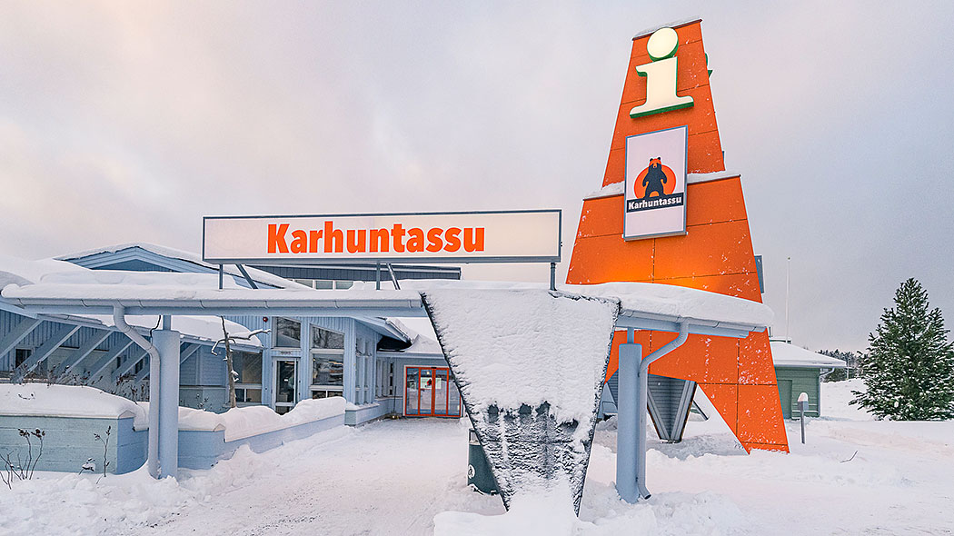 Next to the multifaceted building is a tower-like structure with a large i-sign and other signs. The snow is thin on the ground and on the roof.