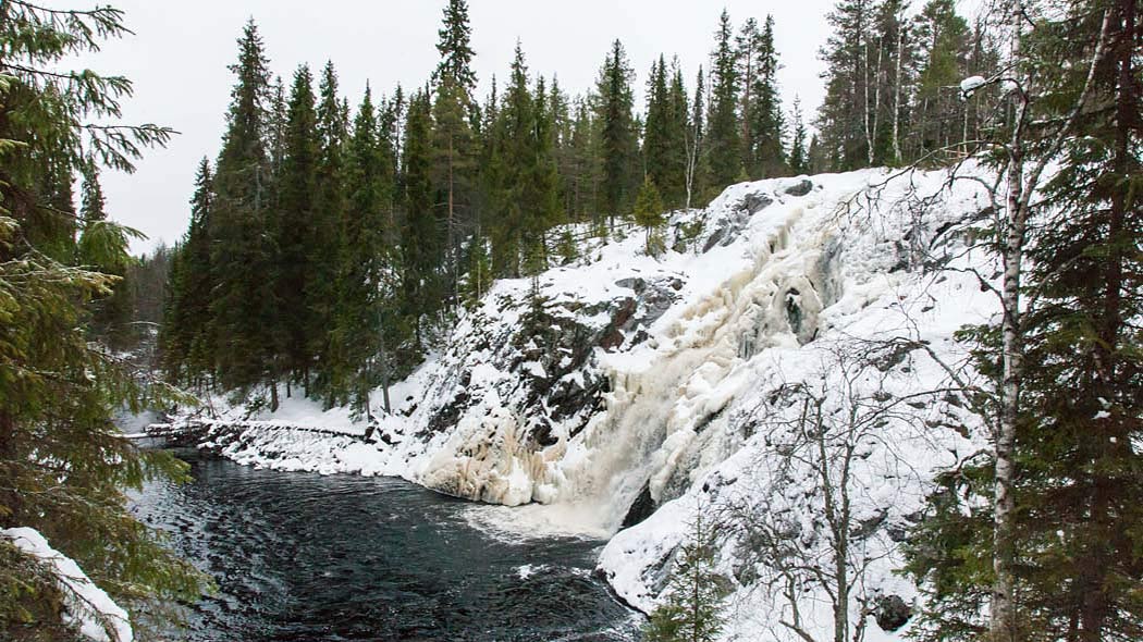 A tall waterfall leading down to the river in a wintry forest.