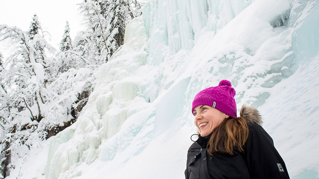 A hiker sits on a snowy slope with her back facing the icefall.
