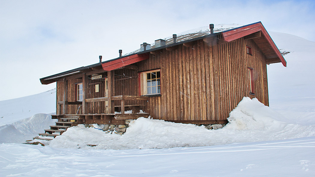 A large cabin with wooden walls on a high natural stone foot in the open winter fell area.