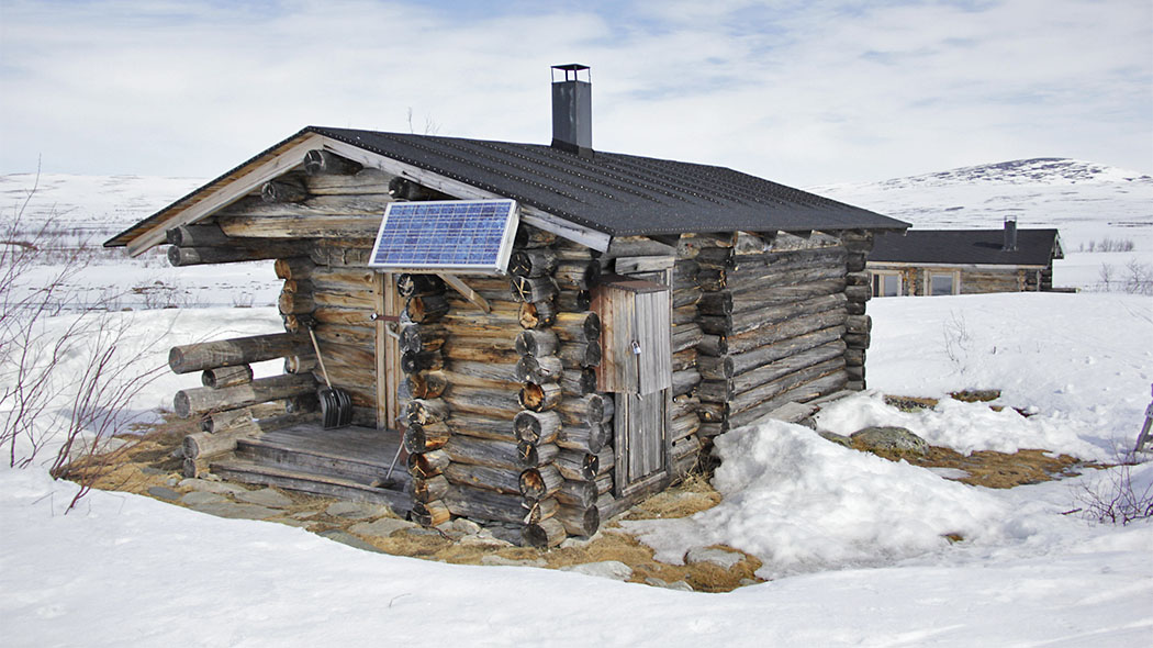 A log cabin in winter. There is a solar panel at the end of the cabin.