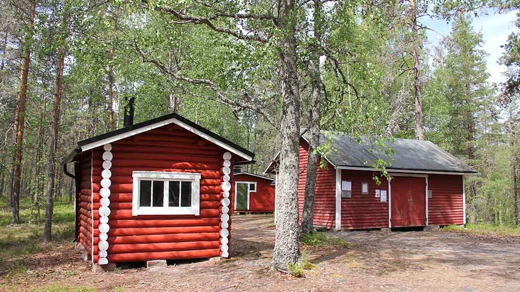 Three small wooden buildings in the woods.