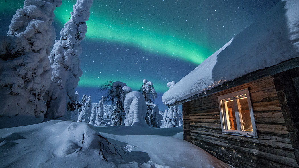 Cottage in a winter forest. There are northern lights in the sky.