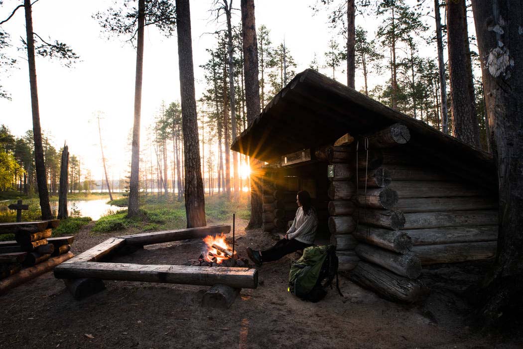 Hiker in the shed by the campfire. In the background a summer evening sunset and a pine forest.