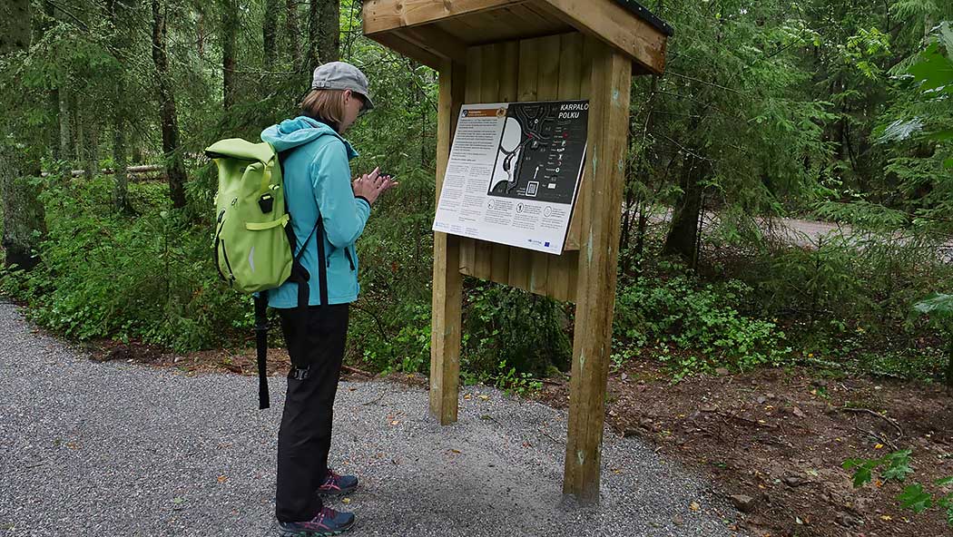 A woman stands on the trail in front of the sign and uses the phone.